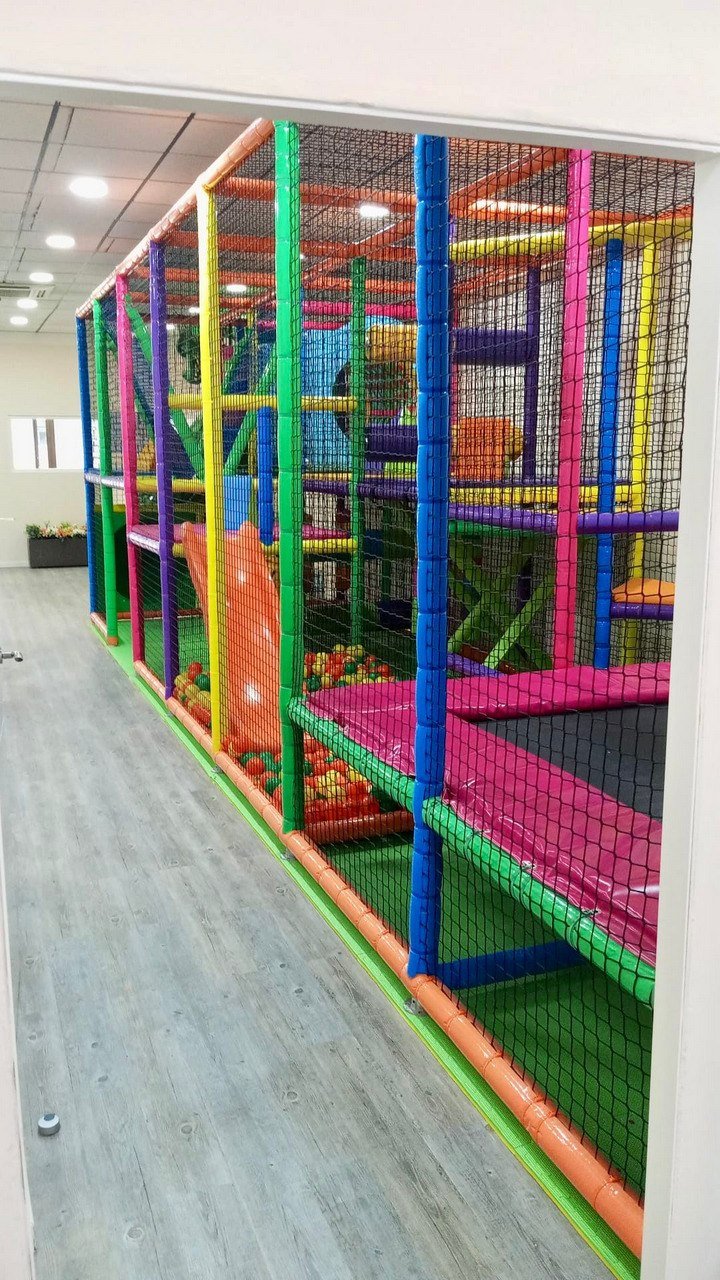 Zona de juegos interior con estructura de colores, piscina de bolas y camas elásticas protegidas.